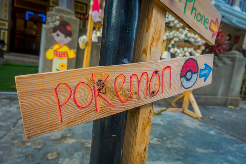 Wooden sign reading “POKEMON” with a Pokéball icon and an arrow, attached to a pole on a street.Pop-culture nod to Pokémon Go’s 2016 moment, when social attention went physical and shared experiences became distribution, a reminder that participation and sharing behaviours drive reach more than “formats”.